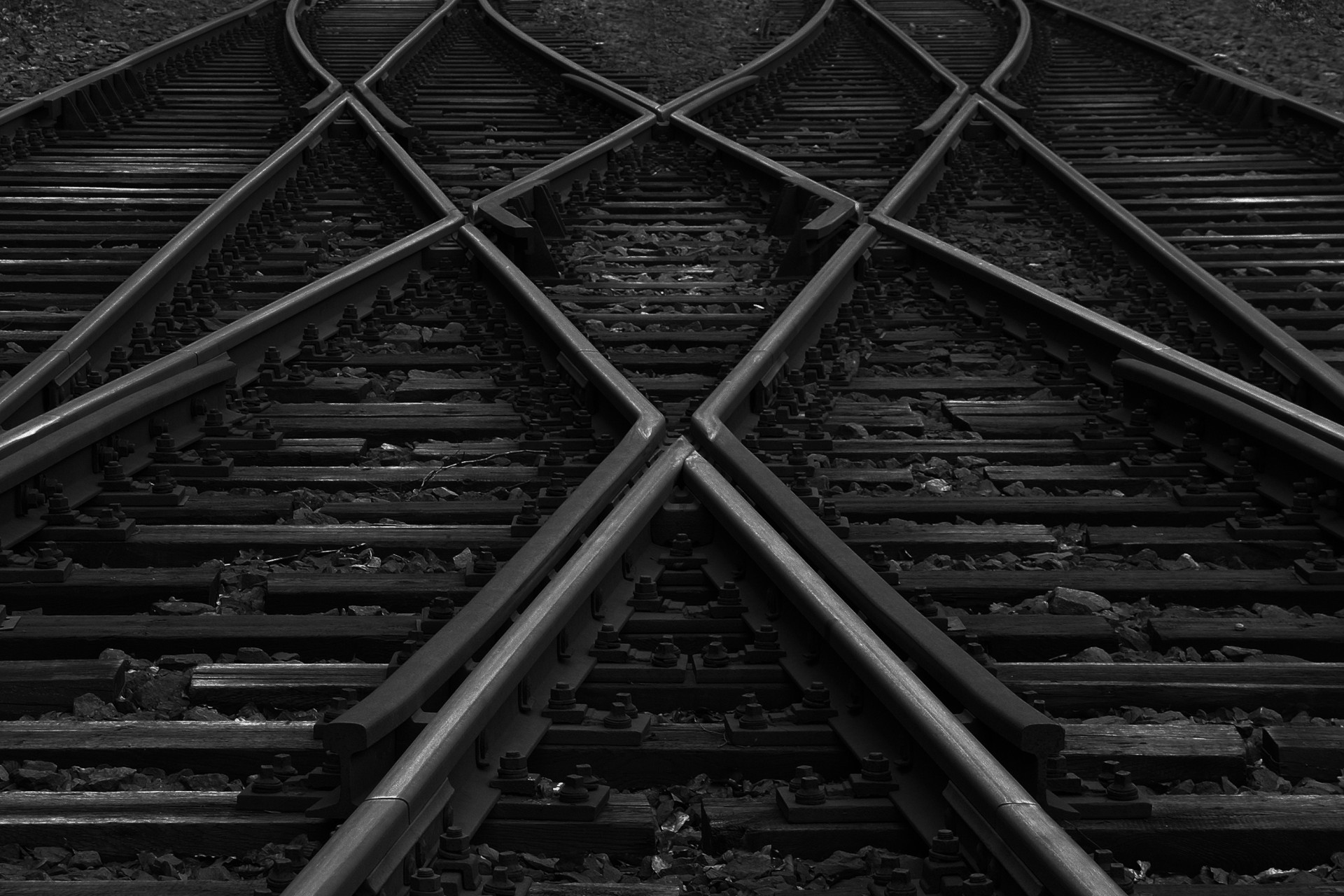 Ein schwarz-weiß Foto von sich kreuzenden Eisenbahngleisen. Die Gleise sind symmetrisch angeordnet und erstrecken sich in verschiedene Richtungen.